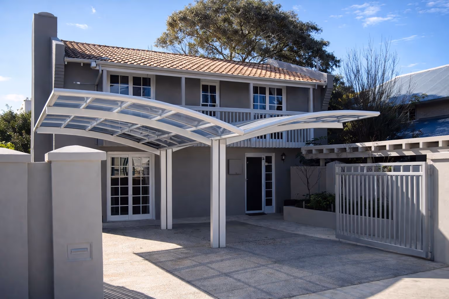 Modern two-story house with a tiled roof and a double carport featuring a curved transparent canopy.